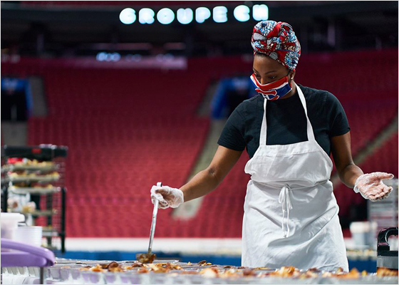 Woman wearing a mask serving multiple meals in an arena.