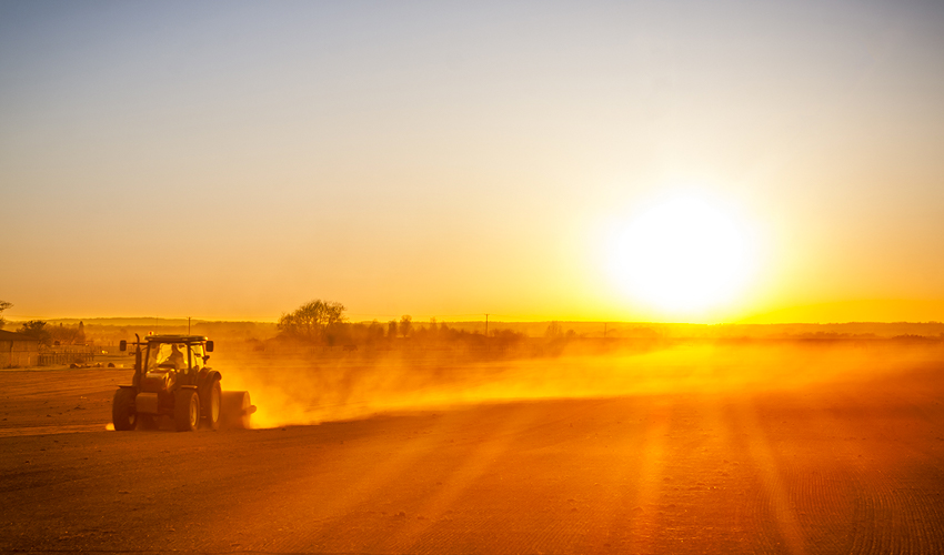 Un fermier conduit un tracteur dans son champ au lever du soleil.