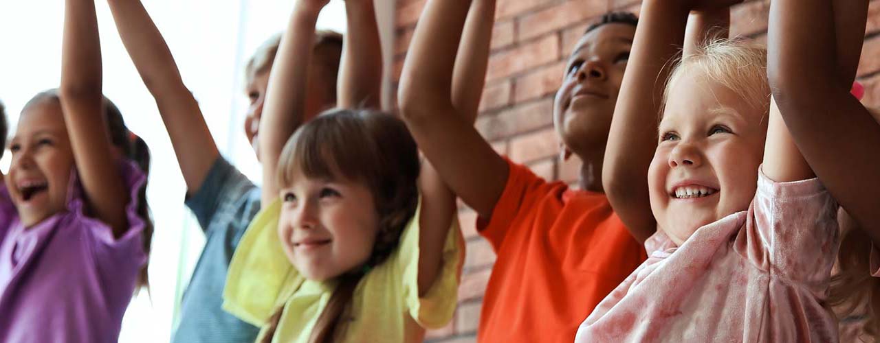 Un groupe d’enfants lève les bras dans les airs en se tenant par la main.
