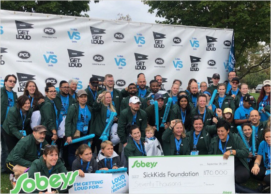 Group of people standing together holding a giant cheque donation for the SickKids foundation