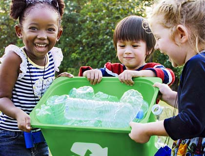 Trois enfants tiennent un bac de recyclage rempli de bouteilles de plastique.
