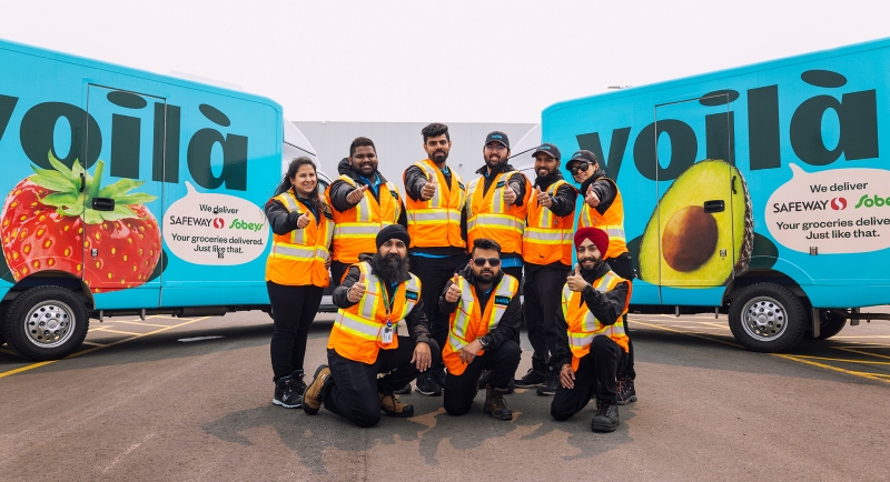 In this image, a group of Sobeys and Safeway employees is taking their picture in front of a Voila van.