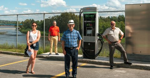 In this image, some people are standing in front of the IGA Ev charger and getting their picture taken.
