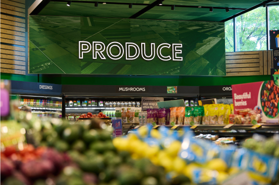 A well-stocked produce section in a grocery store with a prominently displayed "Produce" sign and various fresh fruits and vegetables.