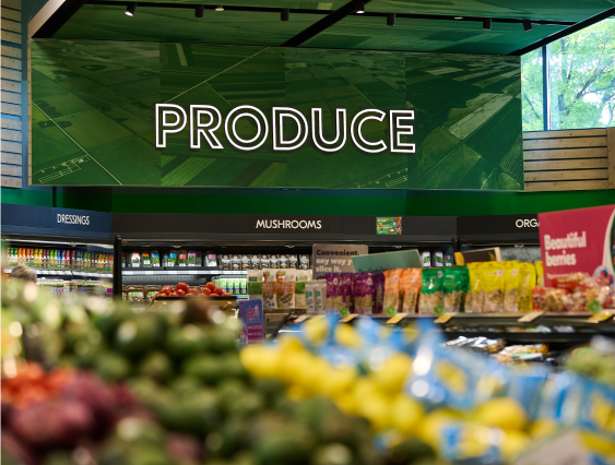 A well-stocked produce section in a grocery store with a prominently displayed "Produce" sign and various fresh fruits and vegetables.
